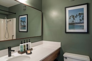 A bathroom with a white sink, a mirror, a framed picture of a beach, and a toilet. - PACIFIC 19 Kona (Kailua-Kona)