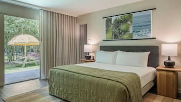 Habitación de hotel con cama, dos mesitas de noche, ventana con cortinas y vista a áreas verdes, además de un cuadro en la pared.