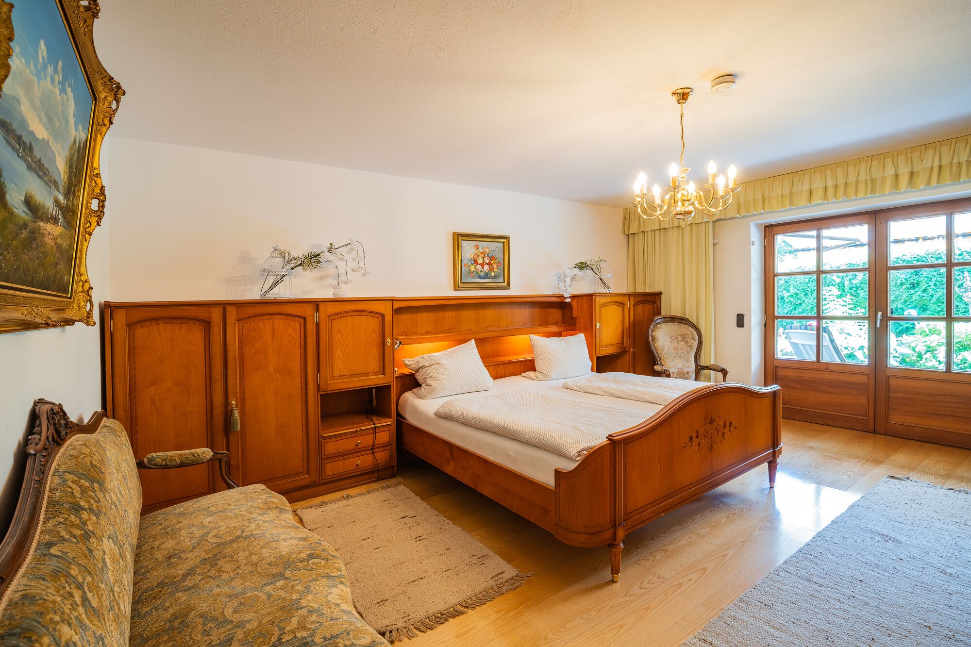 Une chambre à coucher avec un lit en bois, une table de chevet, une chaise, une grande fenêtre et un lustre.