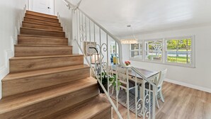 Una escalera de madera con barandillas blancas que lleva a un comedor con una araña.