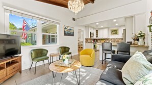 Un salón amplio con televisión, sillones verdes y amarillos, un sofá y una araña.