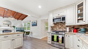 Una cocina moderna con armarios blancos, estufa de acero inoxidable y techo de madera.