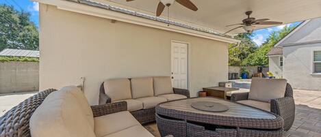 Une terrasse extérieure aménagée avec des meubles en osier, des ventilateurs de plafond et une porte.