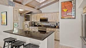 Una cucina con mobili in legno, una grande isola con sgabelli da bar, un forno a microonde e un frigorifero.