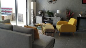 A modern living room with a grey sofa, yellow armchair, and a glass coffee table. There is a large window with a view of a building outside. - Maison 3 Chambres Proche des Plages sur la Presquile de Rhuys (Saint-Gildas-de-Rhuys)