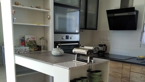 A compact kitchen with a central island, a built-in oven, and a microwave. There are shelves with kitchenware and a coffee machine. - Maison 3 Chambres Proche des Plages sur la Presquile de Rhuys (Saint-Gildas-de-Rhuys)