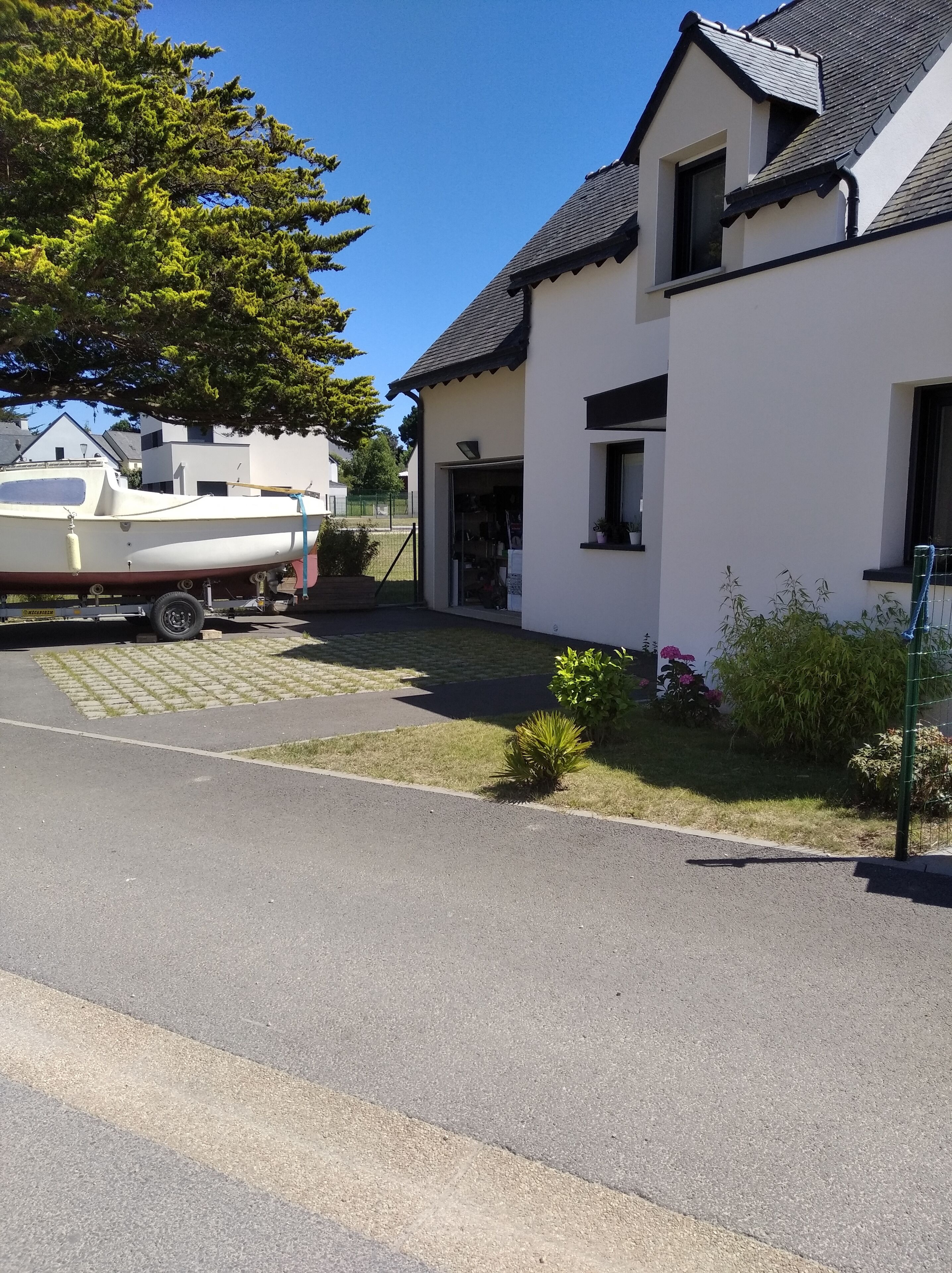A white house with a black roof, a driveway, and a boat parked outside.