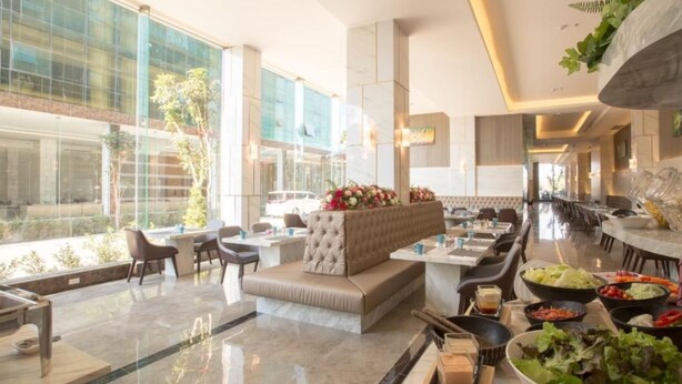 Un lobby de hotel espacioso con una zona de estar, una mesa de buffet con diversos platos y grandes ventanales con vistas al exterior.