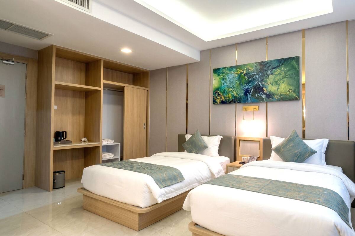 A hotel room with two beds, a wardrobe, a painting, and a nightstand.