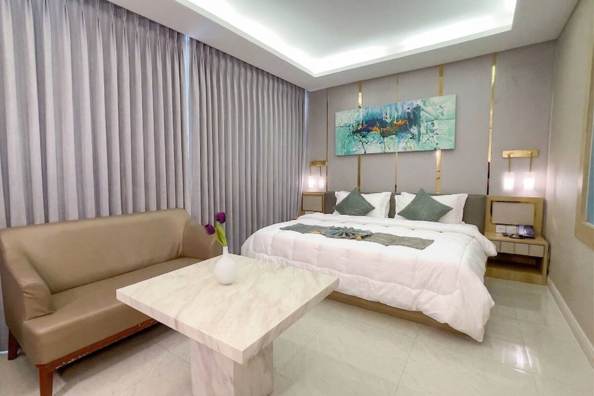 A hotel room with a bed, a sofa, a small table, and a painting on the wall.