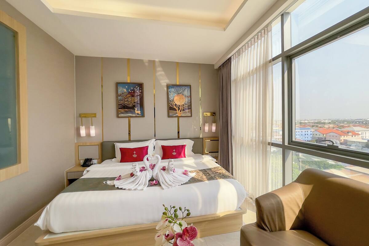 A hotel room with a large bed, two paintings, a view of the city, and a sofa.