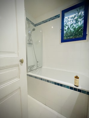 Ein Badezimmer mit Duschkabine, Badewanne und Fenster mit blauem Rahmen.