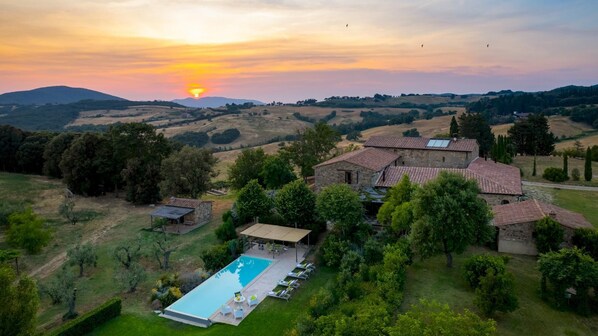 A villa with a swimming pool, surrounded by lush greenery and hills.