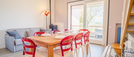 A dining area with a wooden table set for four, surrounded by red chairs, a grey sofa, and a fireplace.