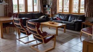 A living room with a sofa, chairs, a coffee table, a bookshelf, and large windows. - Alpine Retreat by Interhome (Adelboden)