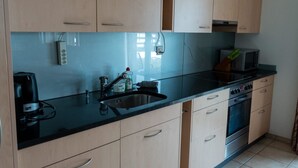 A kitchen with light wood cabinets, a black countertop, a sink, a microwave, and an oven. - Alpine Retreat by Interhome (Adelboden)