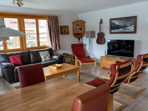 Una sala de estar con un sofá, una mesa de centro de madera, un televisor, una guitarra y un cuadro en la pared.