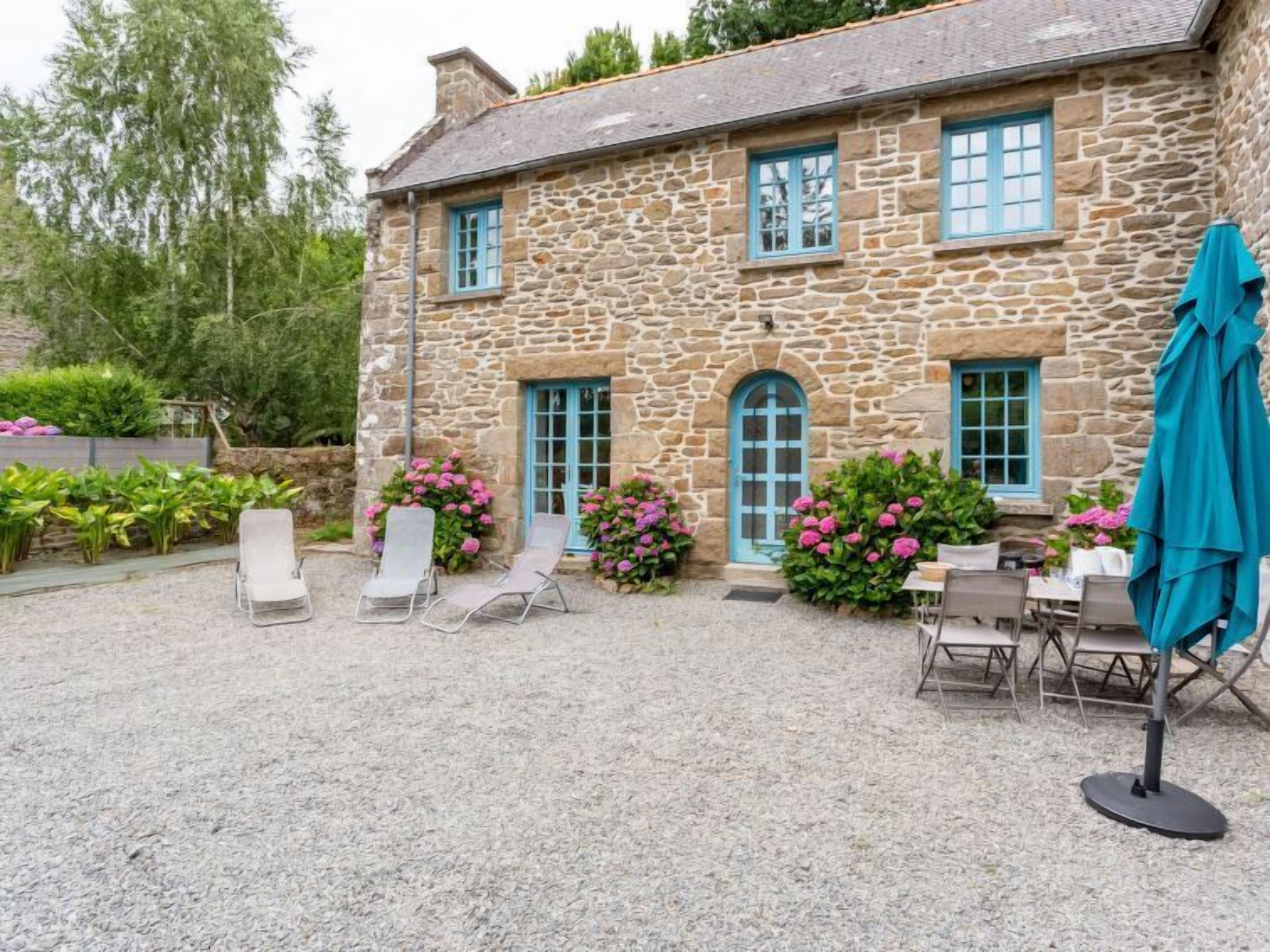 A stone building with a gravel patio, outdoor seating, and flowering plants.