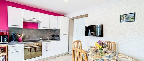 A modern kitchen with white cabinets, a pink accent wall, and a dining area with a patterned tablecloth.