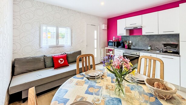 A modern kitchen with white cabinets, a pink accent wall, and a dining area with a table set for two. - Les Bégonias by Interhome (Saint Malo)