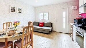 A modern living space with a dining area, a sofa with a red cushion, a kitchen with a microwave, and a patterned wallpaper.