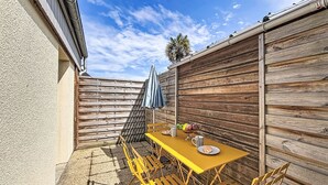 A patio with a yellow table and chairs, a blue umbrella, and a wooden fence.