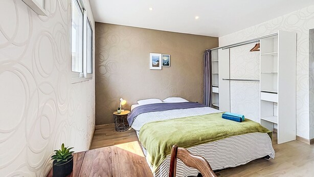 A bedroom with a bed, a bedside table, a lamp, a wardrobe, and a window.