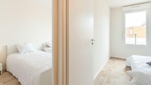 A minimalist bedroom with a large window, a wooden floor, and a white door. - Apartment SC C06 by Interhome (Mimizan)