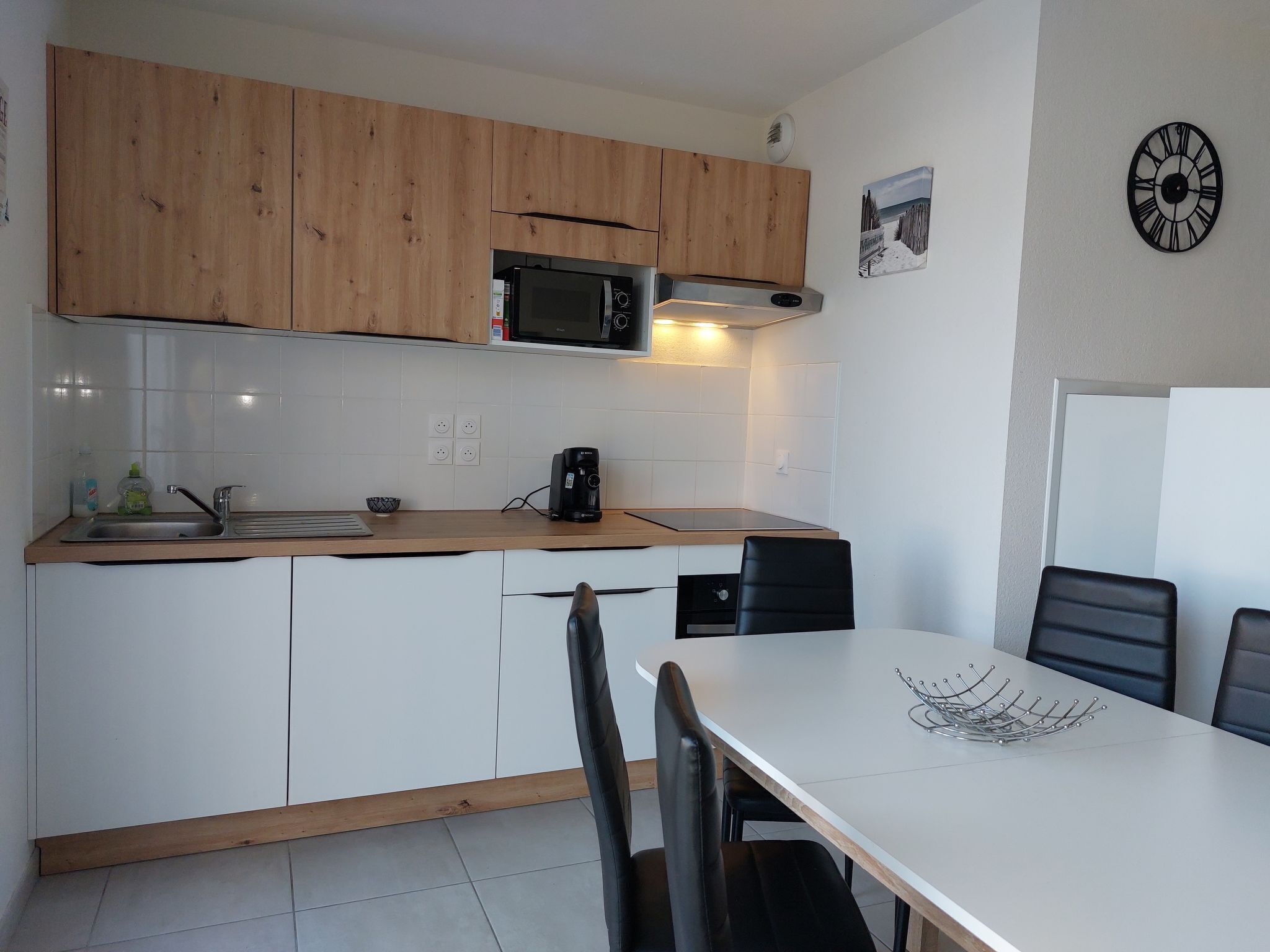 Een moderne keuken met houten kastjes, een magnetron, een koffiezetapparaat en een eettafel met stoelen.