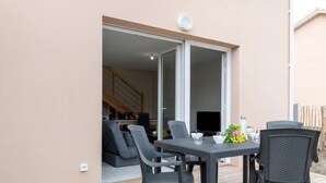 An outdoor patio with a table and chairs, a sliding glass door leading to an interior space, and a wooden deck. - Apartment SC C06 by Interhome (Mimizan)
