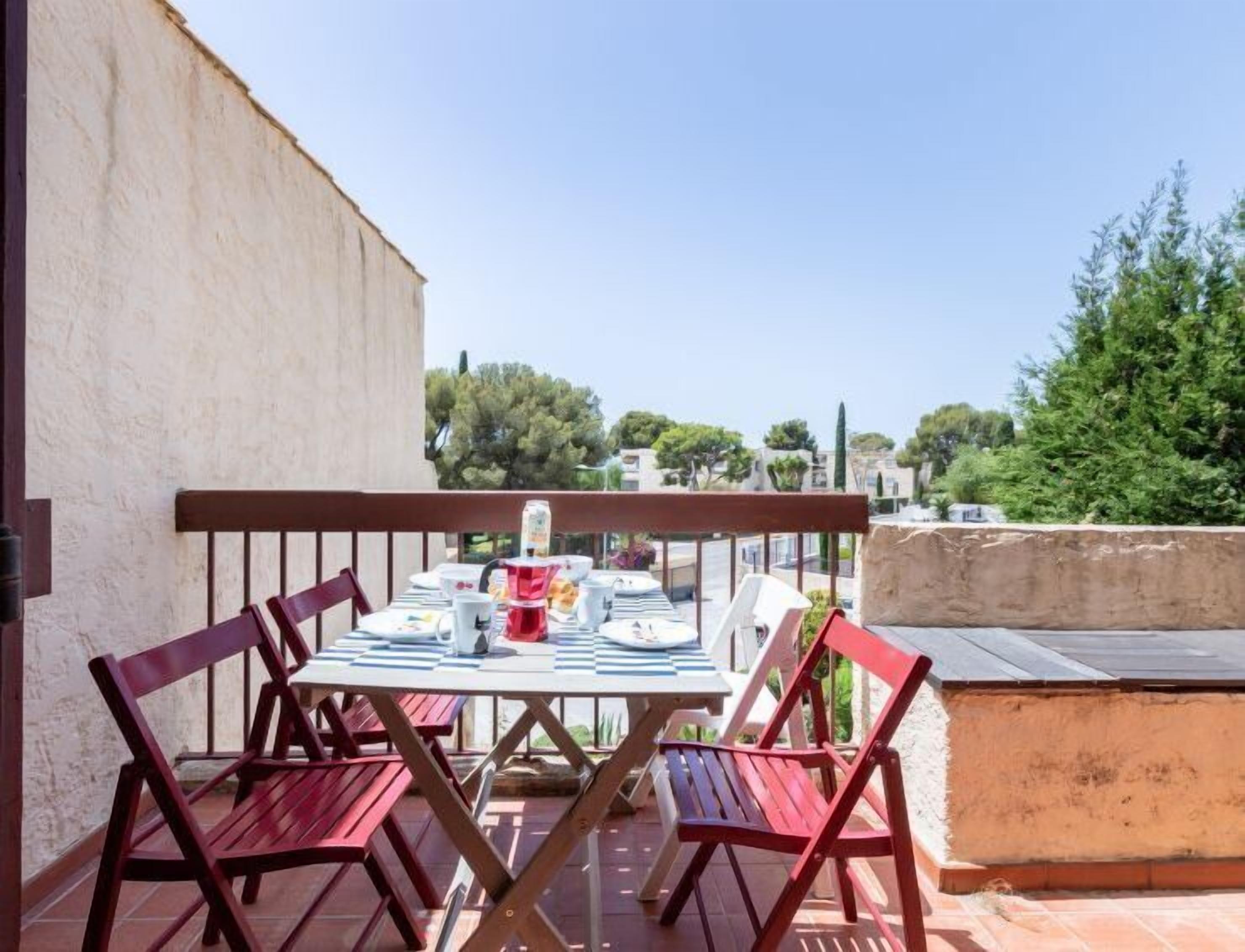 A terrace with a table set for four, surrounded by red chairs, overlooking a residential area with trees and houses.