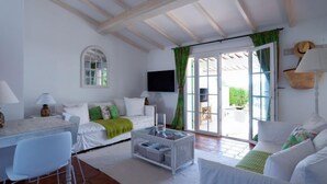 Un salon spacieux avec un plafond haut, un téléviseur fixé au mur et une porte-fenêtre coulissante donnant sur un espace extérieur.