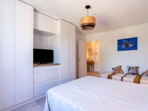 Une chambre à coucher avec un lit, un téléviseur posé sur un meuble, un tableau accroché au mur et une porte donnant sur une autre pièce.