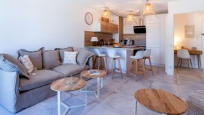 Uma sala de estar moderna com um sofá, duas mesinhas e um espaço de cozinha com banquetas de bar.