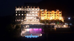 Un hotel de varios pisos con balcones iluminados y un área de piscina.