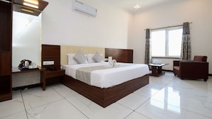 Una habitación de hotel con una cama grande, un cabecero de madera, una mesita de noche, un escritorio, una silla y una ventana con cortinas.