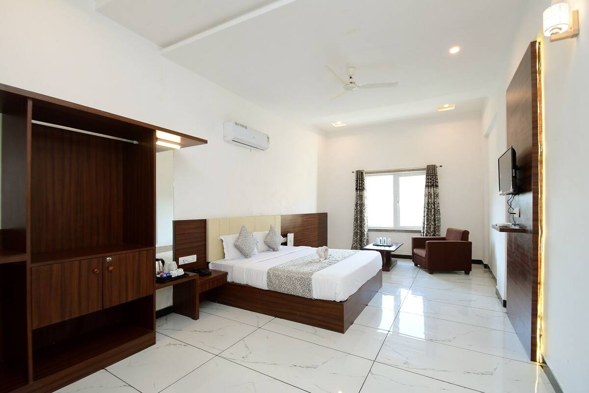 Quarto de hotel com uma cama grande, um guarda-roupa, uma escrivaninha, uma cadeira e uma televisão.