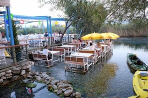 An outdoor dining area with tables and chairs, a small water feature, and a kayak docked by the water. - Hotel Nil (Ula)