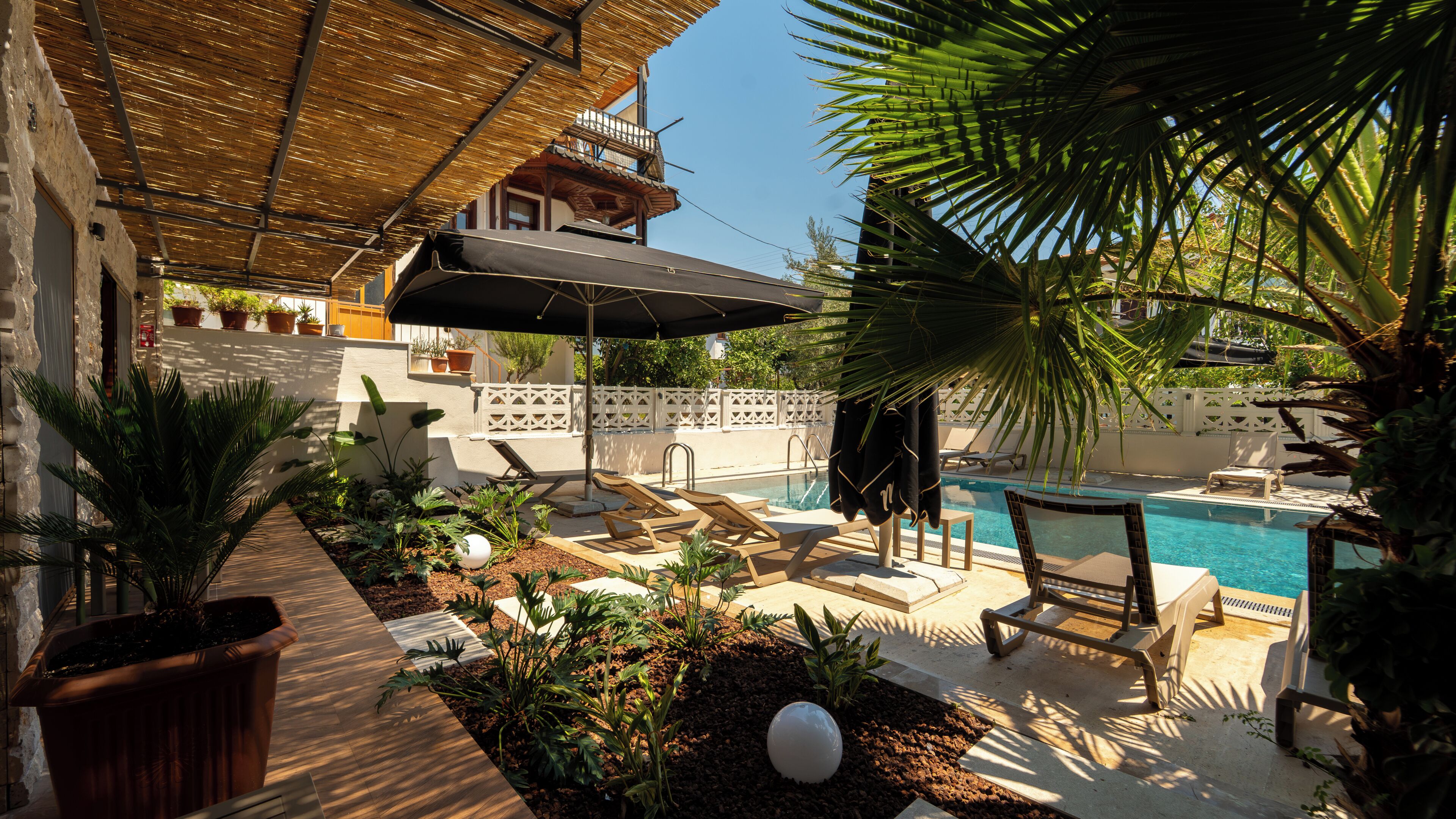 A poolside area with lounge chairs, a pool, and a covered seating area with a thatched roof.