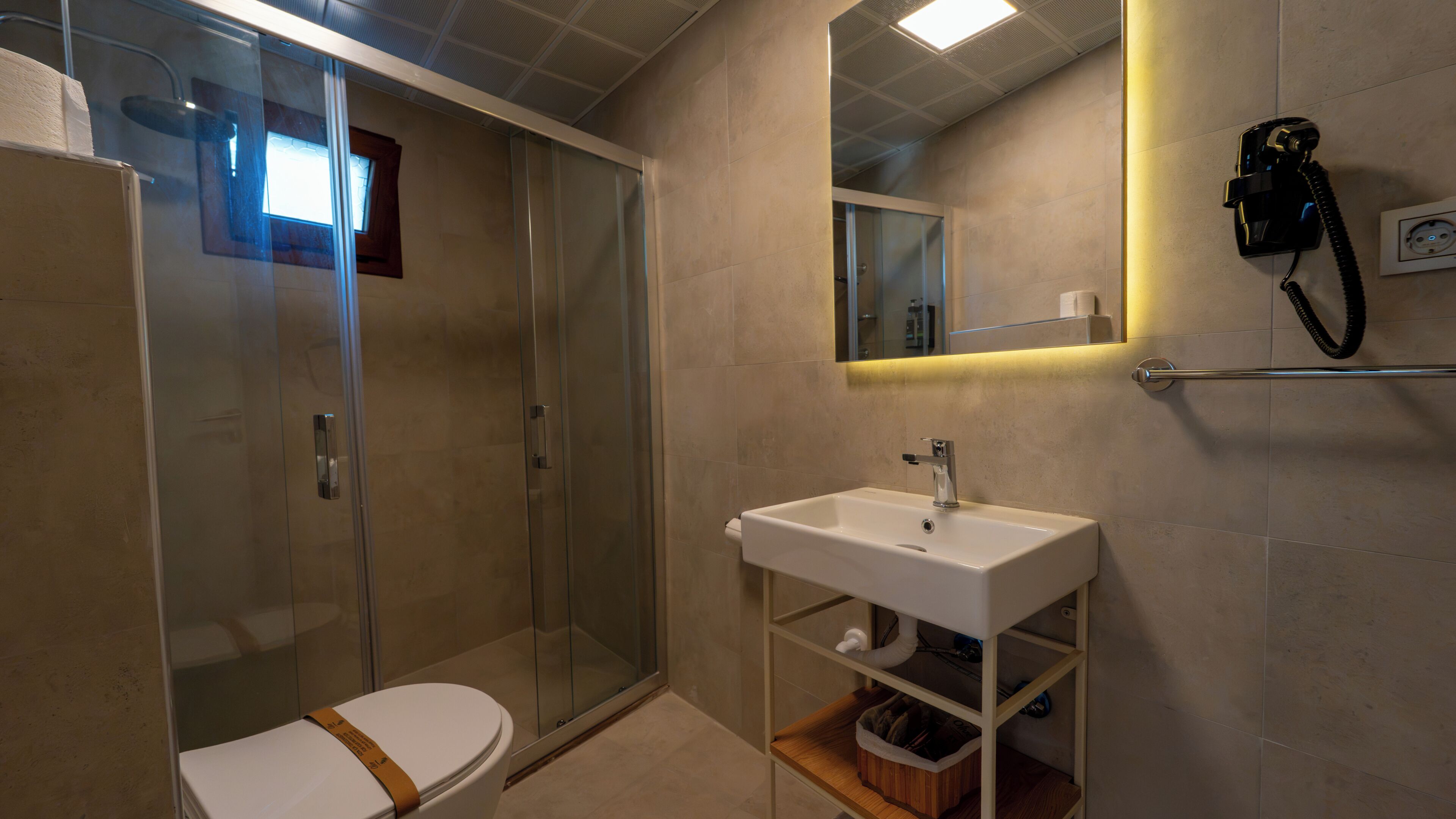Een moderne badkamer met een douchecabine van glas, een wit wastafelmeubel met spiegel en een toilet met een bruine zitting.