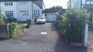 A residential street with houses, a parked car, and a driveway leading to a garage. - Room in shared house in leafy suburban road.  London Zone 4 (Worcester Park)