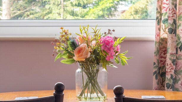 A wooden table with a vase of flowers in front of a window with a view of trees. - Room in shared house in leafy suburban road.  London Zone 4 (Worcester Park)