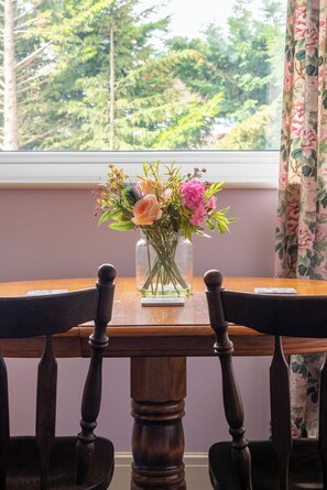 A wooden table with a vase of flowers in front of a window with a view of trees. - Room in shared house in leafy suburban road.  London Zone 4 (Worcester Park)