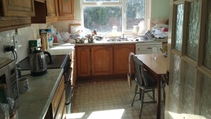 A kitchen with wooden cabinets, a window, and a tiled floor. - Room in shared house in leafy suburban road.  London Zone 4 (Worcester Park)