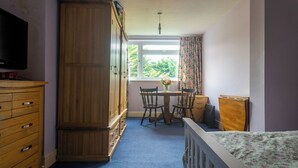 A bedroom with a wooden wardrobe, a desk with chairs, a television, and a window with curtains. - Room in shared house in leafy suburban road.  London Zone 4 (Worcester Park)