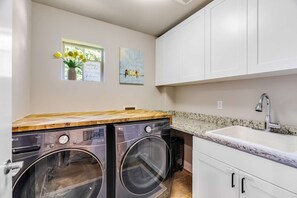 A laundry room with two front-loading LG ThinQ washers, a sink, and a wooden countertop.