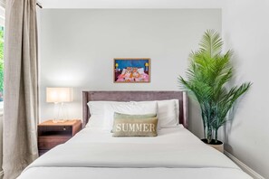 Une chambre d’hôtel avec un lit, une table de chevet, une lampe, un tableau et une plante en pot.