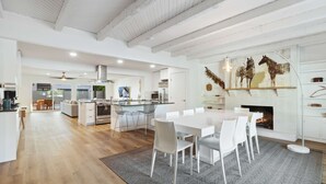 Een ruime woonkamer met een grote eettafel, een keuken met moderne apparatuur, en een open haard.