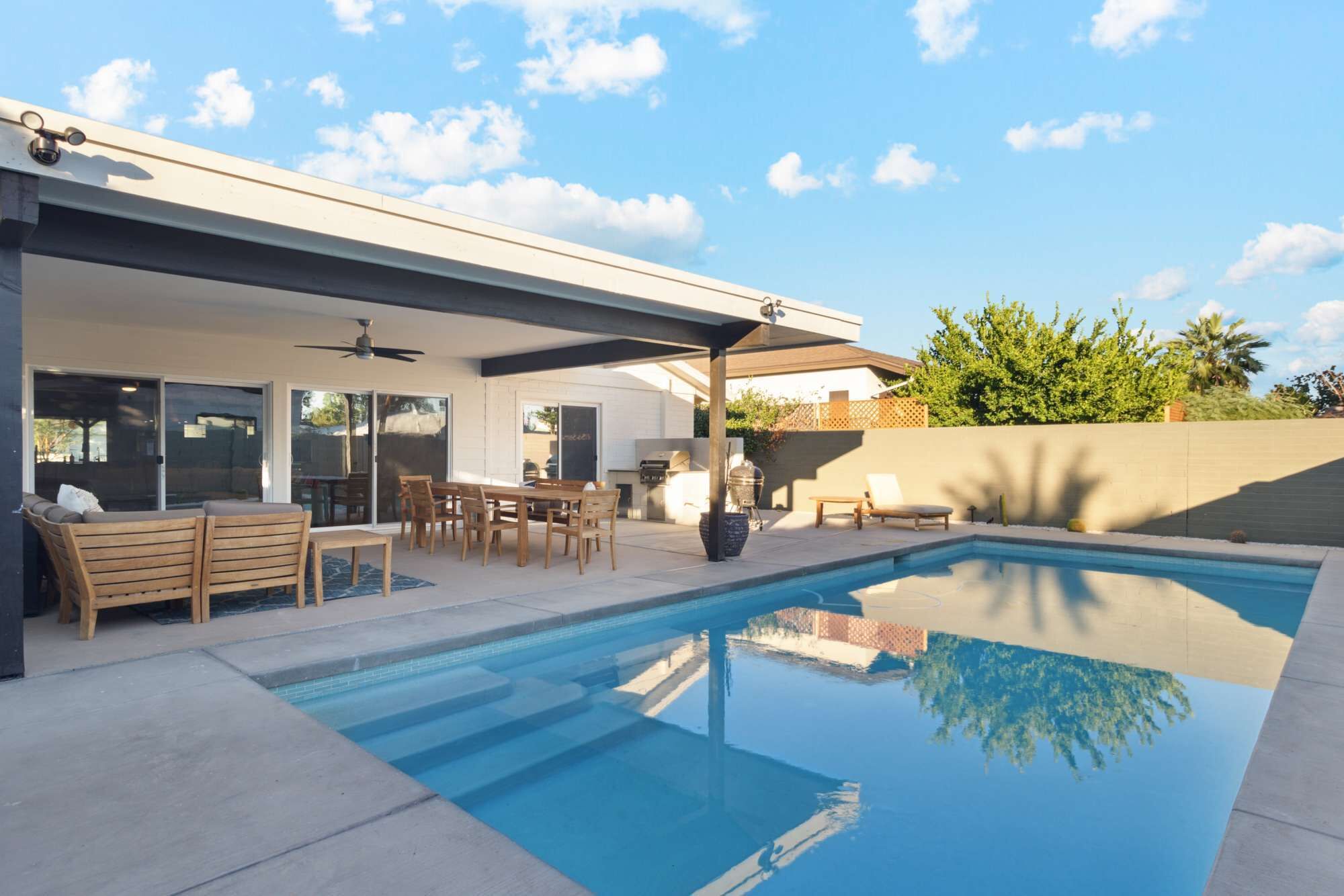 A modern outdoor pool area with a covered patio, seating, and a barbecue setup.