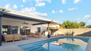 Een modern buitenzwembad met een overdekt terras, zitplaatsen en een barbecuehoek.